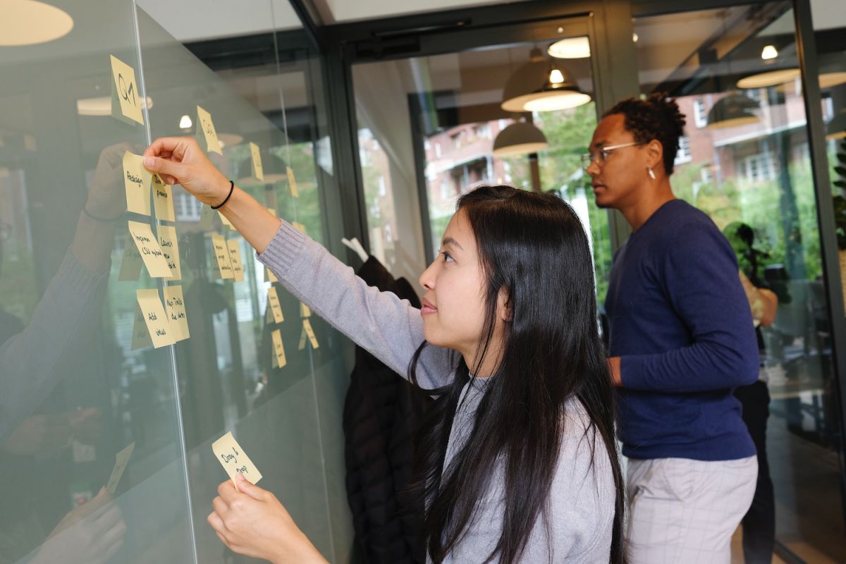 two people add sticky notes to a board