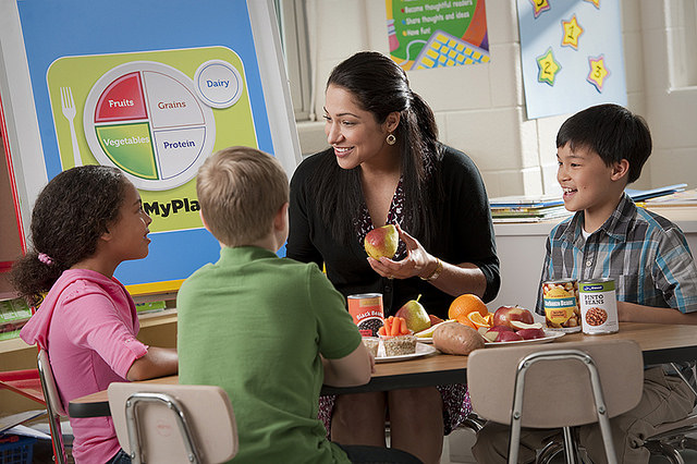 A teacher sits at a table working with a group of three elementary age students.