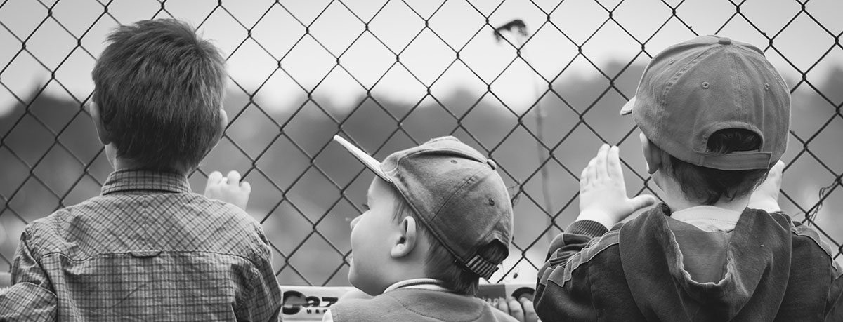 Three boys looking through a chain-link fence