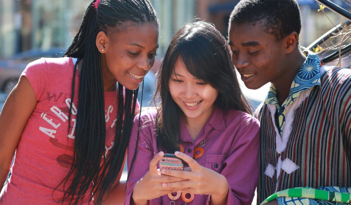 Three teenagers looking at a smartphone and smiling