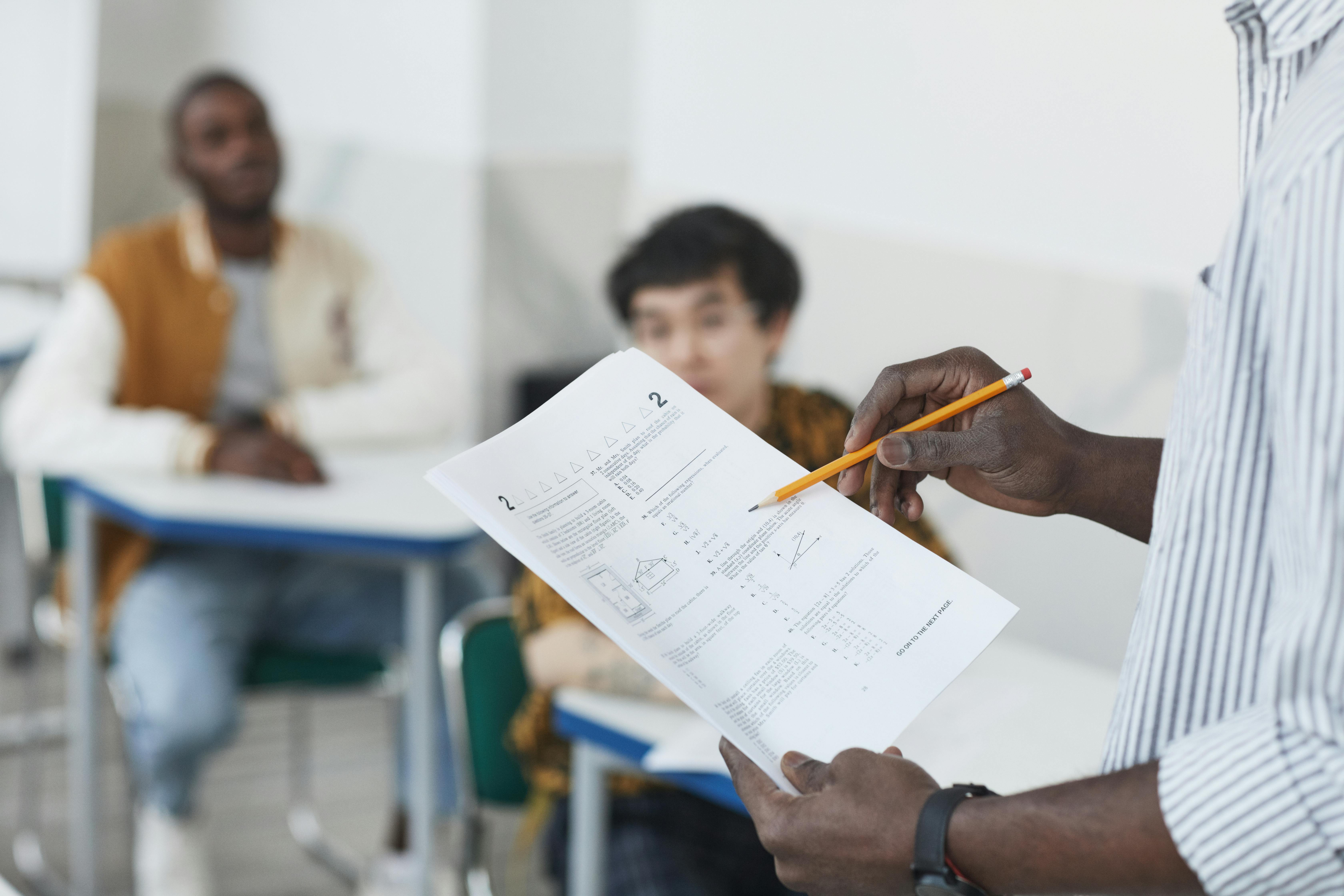 A teacher examines a multiple choice test in front of some students seated at their desks