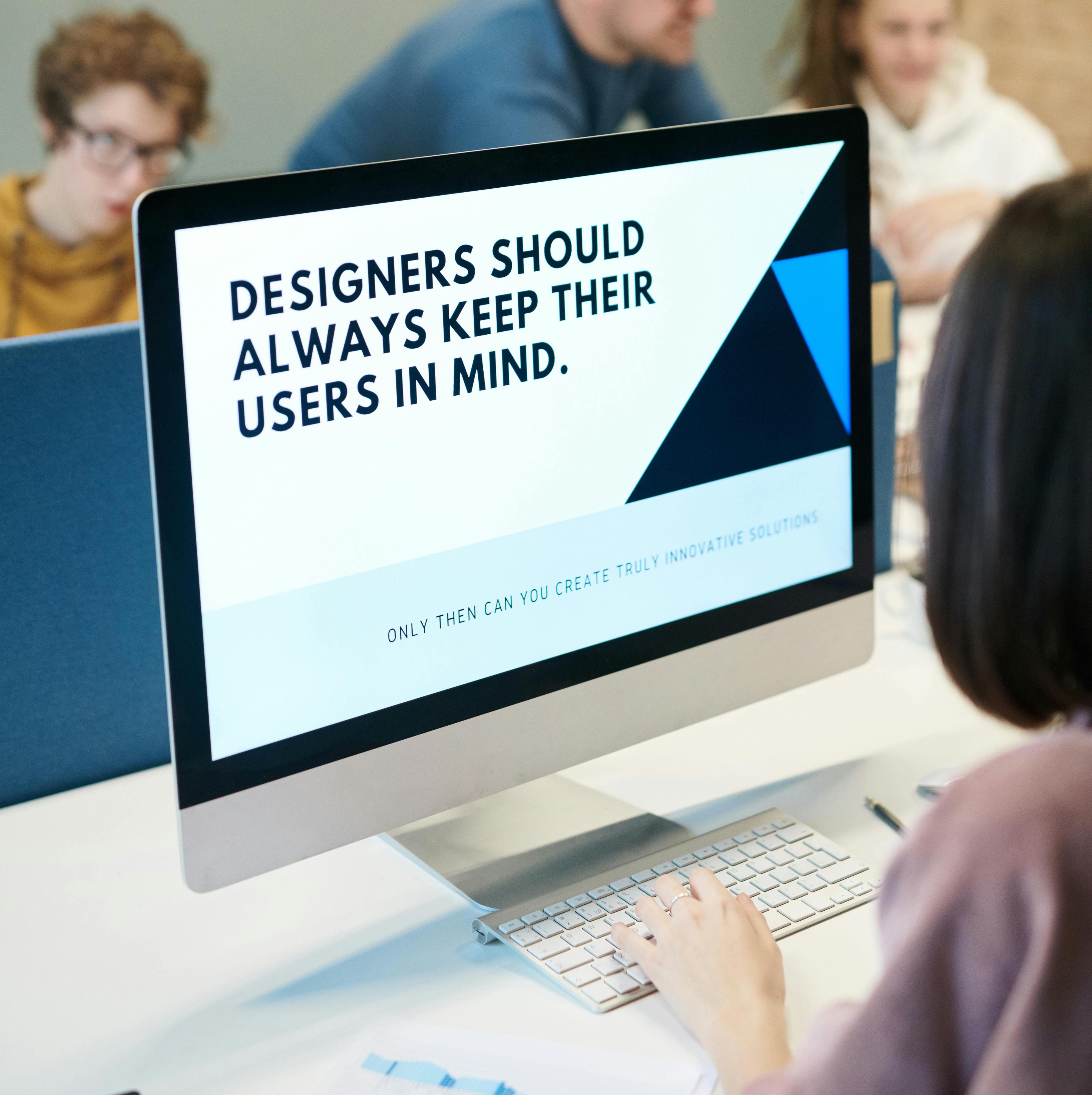 sA woman working on a presentation on their computer. The text on presentation says, "Designers should always keep their user s in mind."
